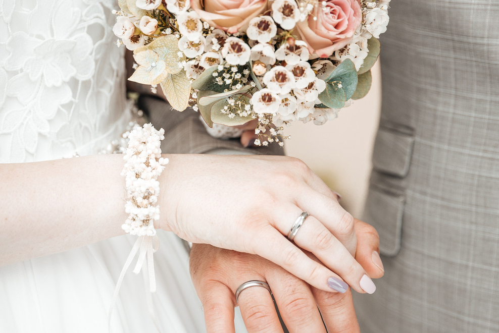 Detail shot of a wedding bouquet and hands of the bridal couple.
